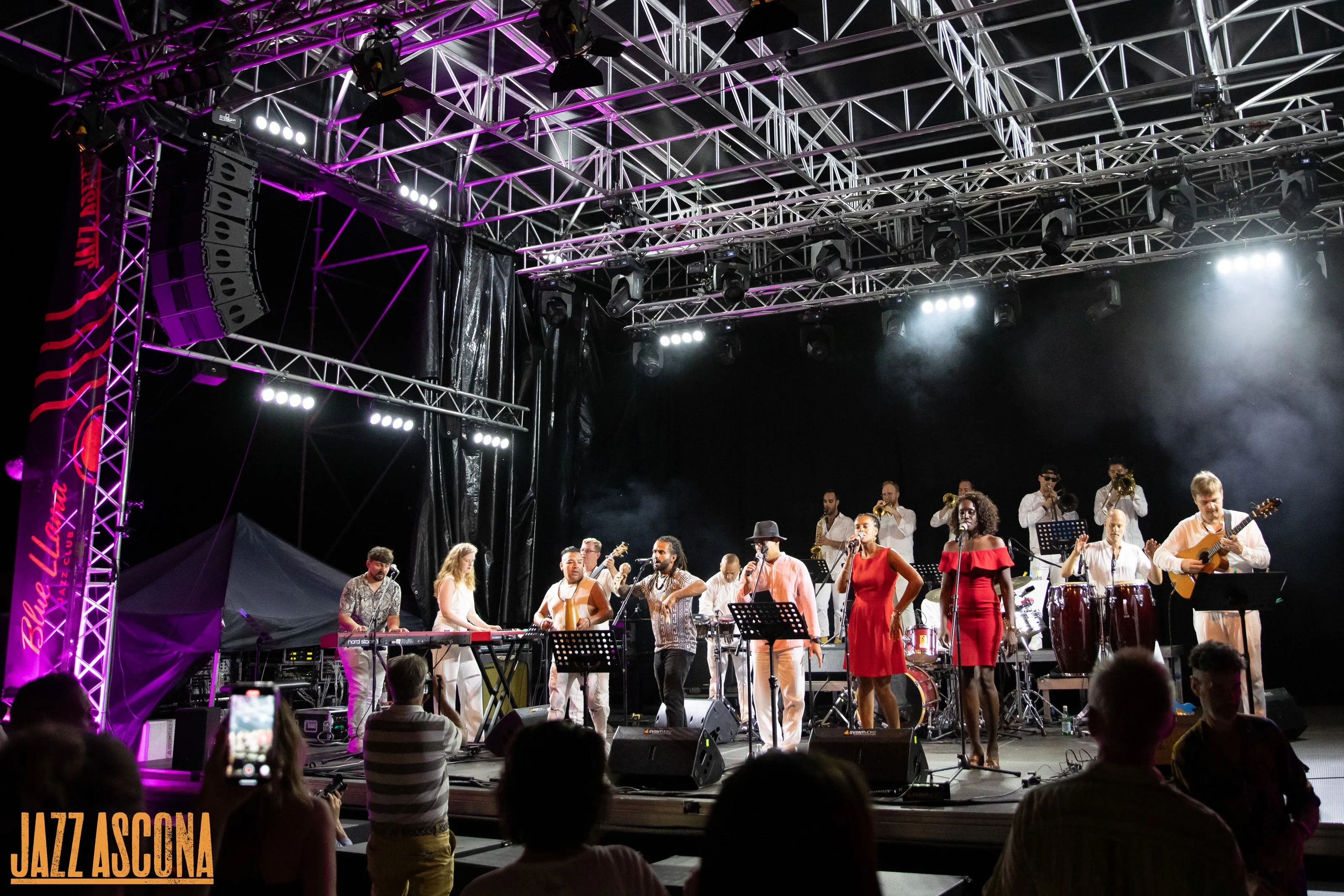 L'orchestre au complet sur la grande scène de JazzAscona — cuivres, chanteuses en rouge et congas sous la charpente de lumières